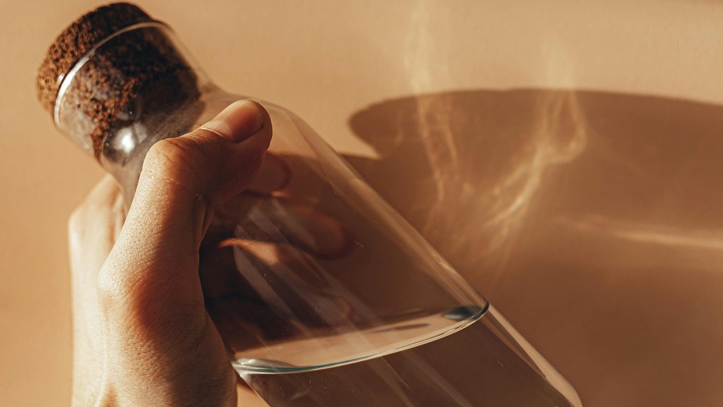A person holding a glass water bottle with water in it.