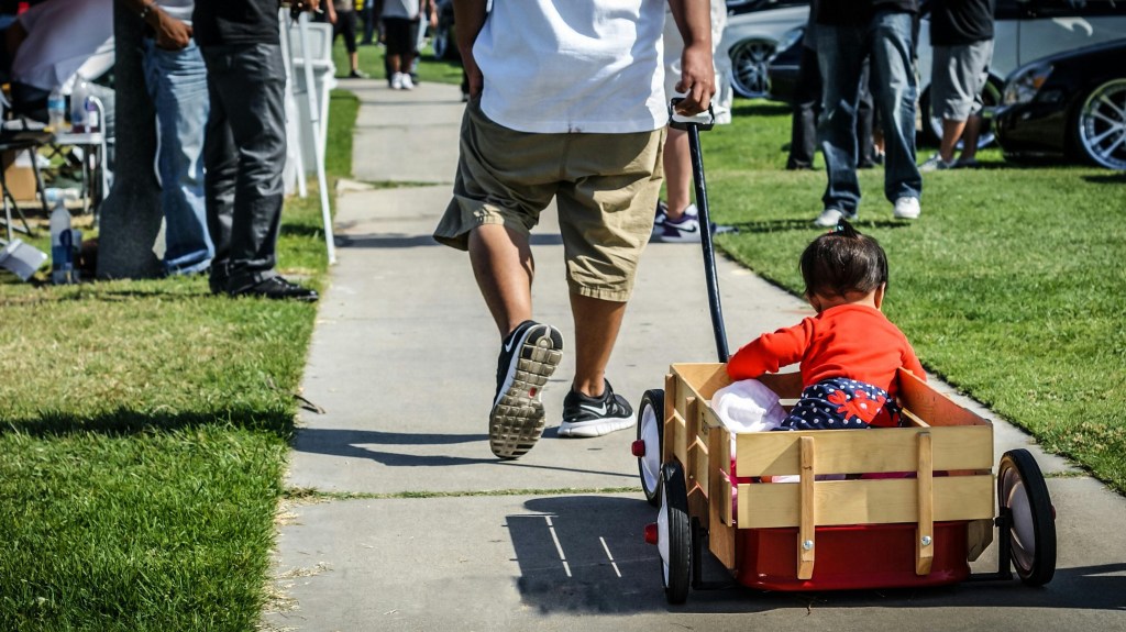 A man pulling his infant child in a wagon behind him at an event.